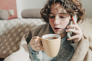 Woman sitting on chair, keeping warm with blanket over shoulders and hot chocolate